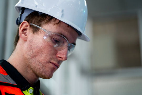 A man wearing a hard hat and safety glasses is looking at something - Powered by Adobe