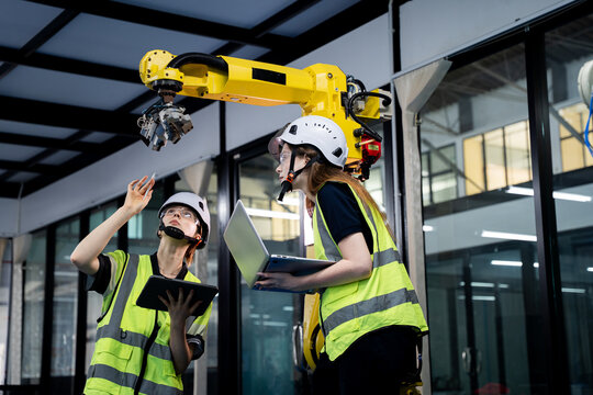 Two people in yellow vests are working on a robot