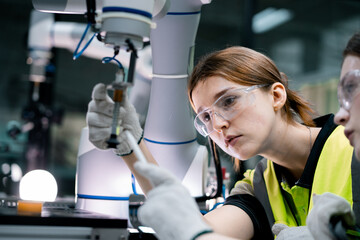 Two women wearing safety goggles and yellow vests are working on a machine