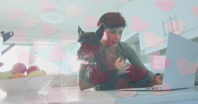 mid-adult woman showing love to dog at kitchen while scrolling trackpad, generating heart graphics