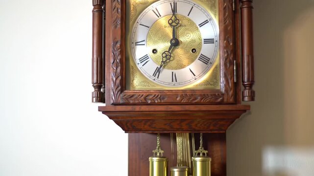 A close-up shot of a grandfather clock with a white and gold face, roman numerals, and a wooden frame