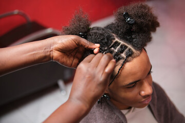 Top view of smiling afro young man getting meticulously braided hair
