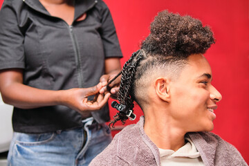 Afro young man smiling while stylist braids his hair from behind