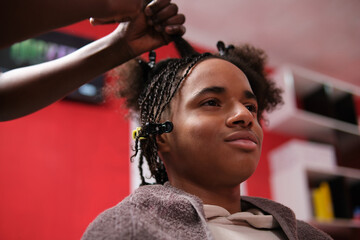 Afro young man semi-profile with half braided hair and hairstylist hands