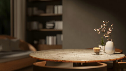 Coffee cup with pot plant and flower vase on round marble table with sofa and bookshelf in dim room.