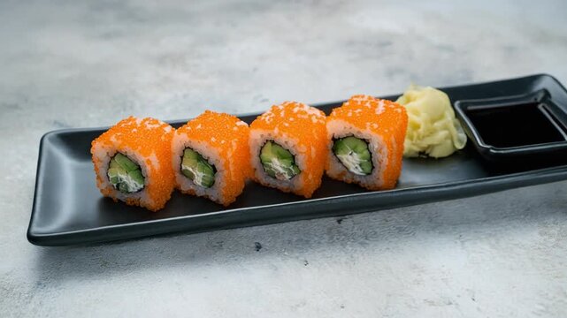 Masago sushi rolls orange, slow 360-degree orbit shot of sushi topped with bright orange fish roe, cucumber, and cream cheese on a long black plate.