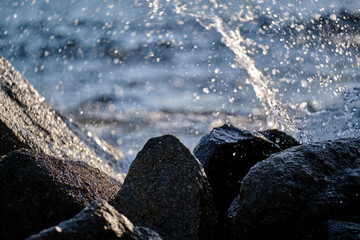 Water splashes against rocks near the shore in bright sunlight during the day