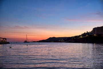 Sunset over the ocean with a boat in view near the shore of a coastal town