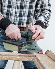 Craftsman. Adult carpenter using an electric sander to smooth an old wooden window. Construction industry, carpentry, housework do it yourself. Restoration.