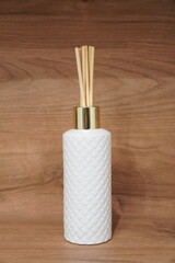 Elegant white diffuser bottle with gold accent and natural reeds on a wooden background