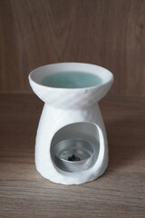 White ceramic oil burner with tealight candle and blue water on a wooden surface