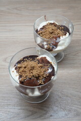 Two elegant glasses of creamy dessert topped with chocolate sauce and cookie crumbs