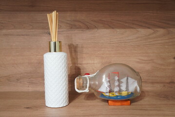 Decorative reed diffuser and ship in a bottle on a wooden shelf