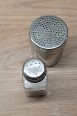Two salt and pepper shakers, one glass and one metal, sit on a wooden table