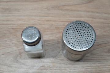 Two salt and pepper shakers, one glass and one metal, on a wooden table
