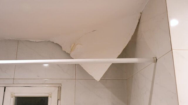 Severe water damage in a bathroom: Paint peels off the ceiling due to heavy humidity and water infiltration. Renovation and insurance claim concept.