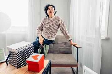 A young Asian woman with short black hair sits on a chair, red gift box in a cozy indoor setting. Winter Holidays: Christmas and New Year