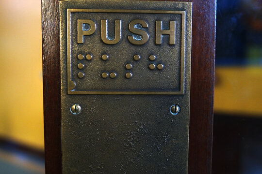 Vintage Brass Push Plate with Braille Text on Dark Wood Door, Tactile Accessibility Signage
