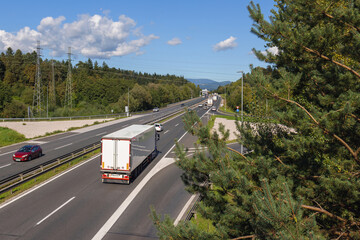 Truck travel along a highway amid trees, showing vital transport routes for goods and e-commerce logistics in economic activity.