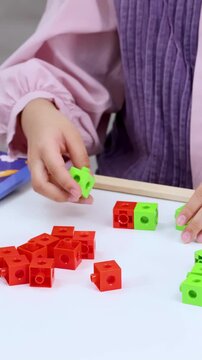 Child Hands Connecting Red and Green Math Manipulative Cubes on Table