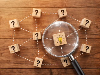 Magnifying glass focusing on lightbulb idea block surrounded by question mark blocks on wooden table