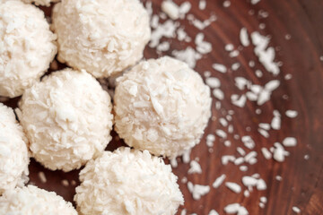 Soft spherical sweets coated in coconut flakes on a dark wooden surface