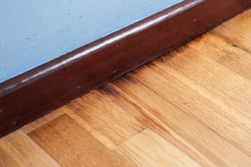 Damaged laminate flooring near a blue wall and wooden baseboard by moisture exposure in a residential room. Humidity impact with material deterioration