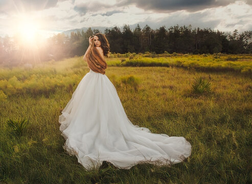 Young woman in a strapless dress and fake fur shrug standing in a rural landscape
