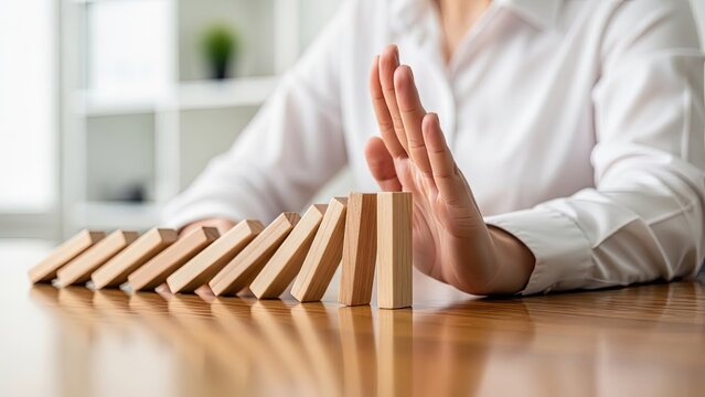 Businesswoman stopping domino effect with hand to prevent crisis and risk.