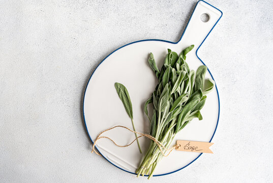 Overhead view of a bunch of fresh sage tied with string and a tag with the word sage on a chopping board