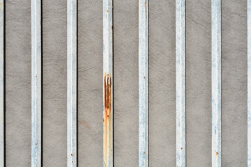 A straight view of several vertical white metal bars with rust spots mounted against a textured grey stone surface