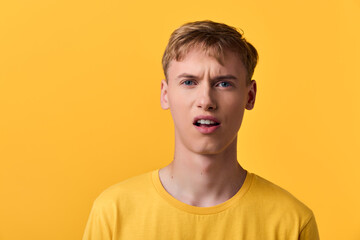 Fototapeta premium Young man in yellow shirt with puzzled expression against a bright yellow backdrop, conveying confusion, uncertainty, or questioning emotions in a studio setting.