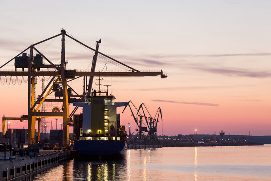 Silhouette of a Container ship moored alongside container cranes in the port at sunset, Klaipeda, Lithuania