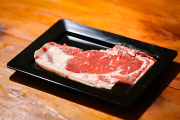 Fresh Cut of Ribeye Steak: A delectable, raw ribeye steak is artfully presented on a sleek black...