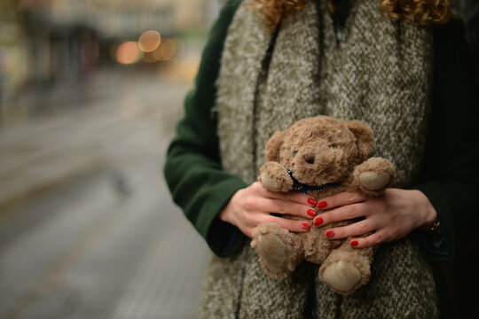 Close-up of a young woman in a coat and scarf standing in a street holding a teddy bear