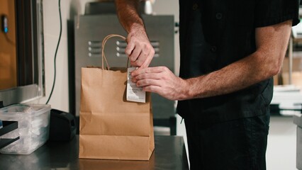 Chef preparing food delivery order, attaching receipt to a takeout paper bag