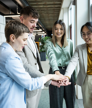 Colleagues stack hands celebrating teamwork success in modern office