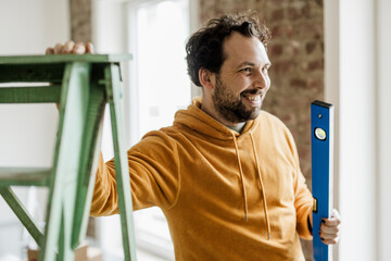 Smiling adult in orange hoodie renovating home with level tool indoors
