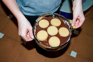Chocolate biscuit cake preparation in glass dish overhead in kitchen