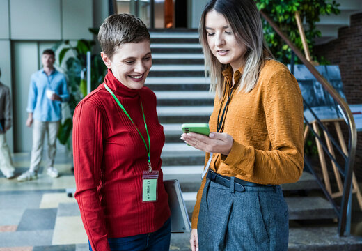 Two colleagues discussing work using a smartphone in a modern office