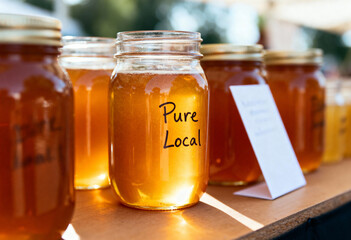 Jars of pure local honey on display at a farmers market. Artisanal golden honey in glass jars for sale. Natural organic food from a small business