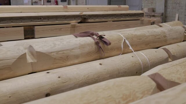 Cylindrical wooden logs with smooth surfaces and unique grain patterns are bundled with straps in a workshop, ready for use in building or transport
