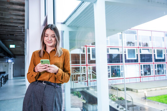 Smiling woman with mobile phone in modern office next to large window