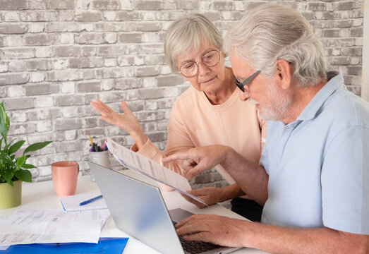 Happy senior couple using a laptop together at home, looking at the screen while managing paperwork. Concept of active aging, digital literacy, online banking, communication, technology - Powered by Adobe