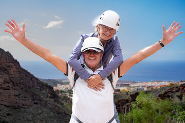 Smiling senior couple of hikers with helmets enjoying a trekking day on mountain - Carefree climbing tourists enjoying holidays, healthy lifestyle, freedom, sport. Horizon over sea