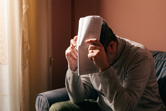 Stressed man overwhelmed by paperwork while working on the couch at home