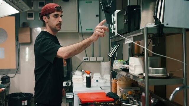 Chef interacting with a digital tablet and microwave in a ghost kitchen, preparing food