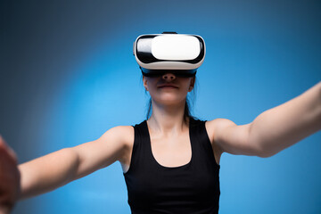 Young woman in virtual reality headset interacting with digital space, immersive VR technology concept on blue background