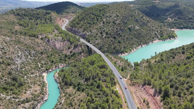 Aerial view of a long bridge stretching over a turquoise river cutting through hills covered with lush green trees, El Grado, Aragon, Spain.