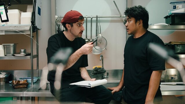 Chef manager explaining cooking workflow to employee in dark kitchen